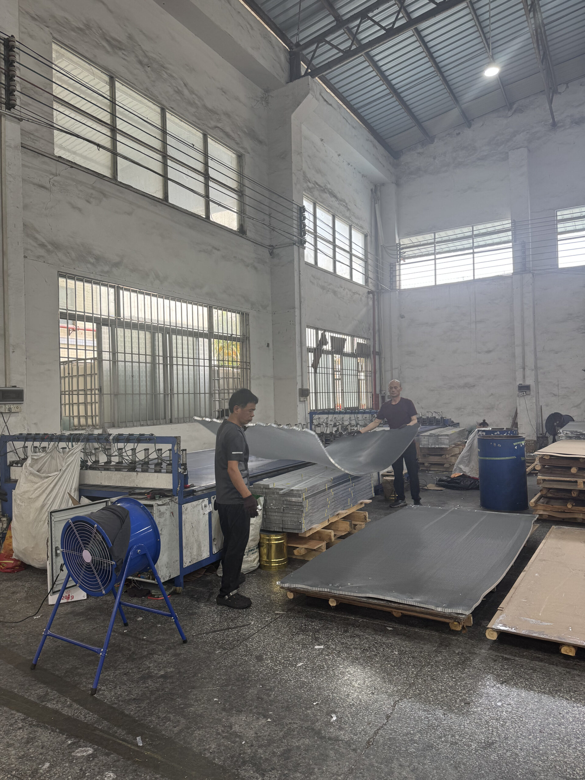 Workers handling aluminum honeycomb core sheets in a manufacturing workshop